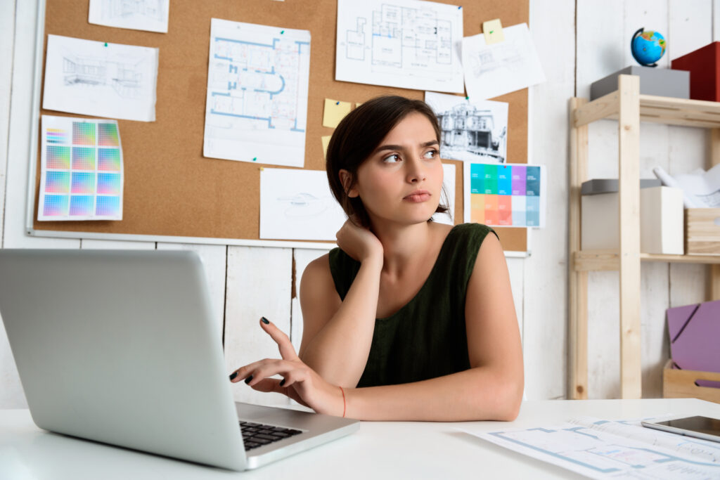 A young professional working on guest post backlinks strategy at her desk, using a laptop, with design plans pinned on the wall.